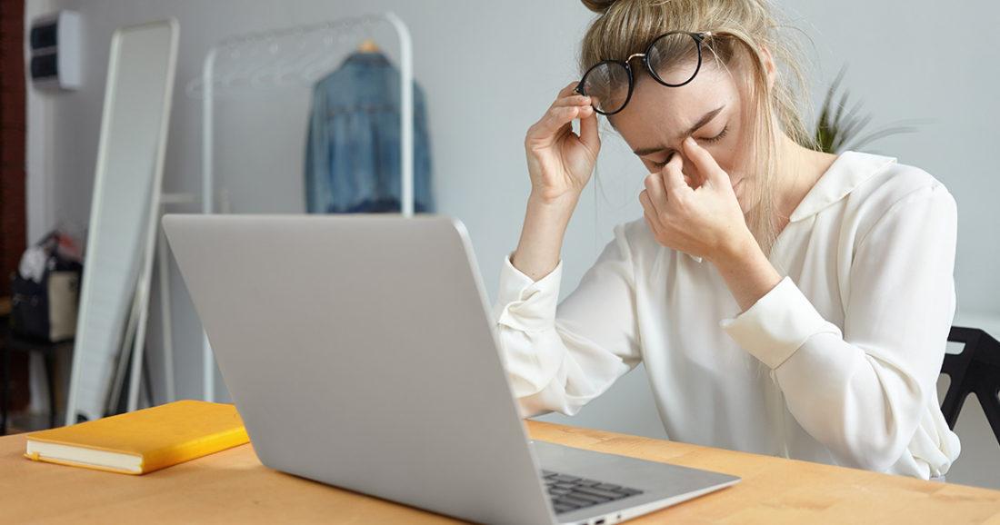 Una mujer está sentada en un escritorio con una computadora portátil y experimenta fatiga visual.