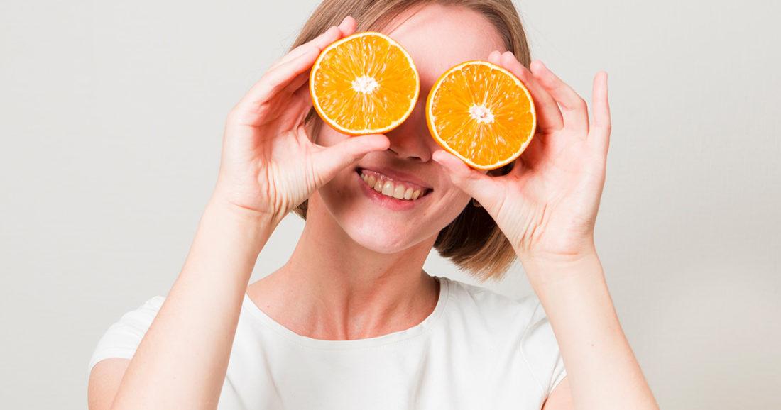 Una mujer sosteniendo rodajas de naranja frente a sus ojos promoviendo la alimentación saludable y la nutrición visual